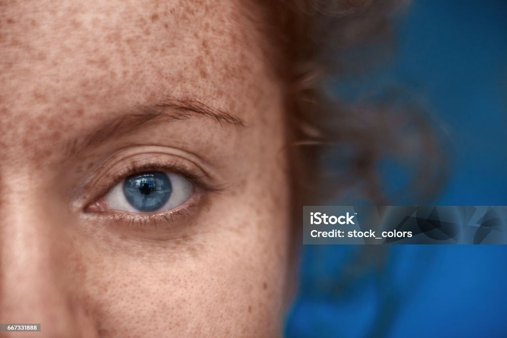 blue eye macro close up shot of woman with blue eye looking at camera, freckels on her skin, red hair. Blue Stock Photo