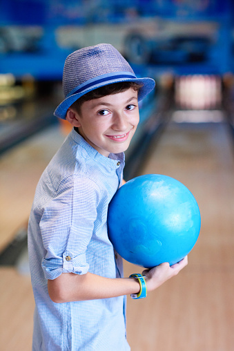front view of little boy holding blue bowling ball and smiling at camera, ready for playing.