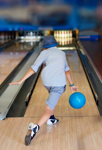 rear view of little boy throwing bowling ball with speed, leisure activity.