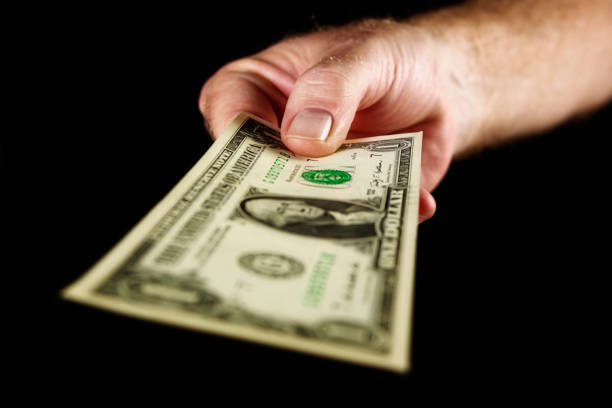 istock Male hand offers US one dollar banknote against black 667357768