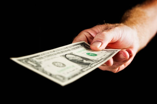istock Male hand offers US one dollar banknote against black 667359946