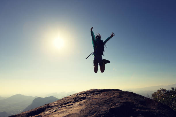 istock cheering successful young woman hiker jumping on mountain peak 667361382
