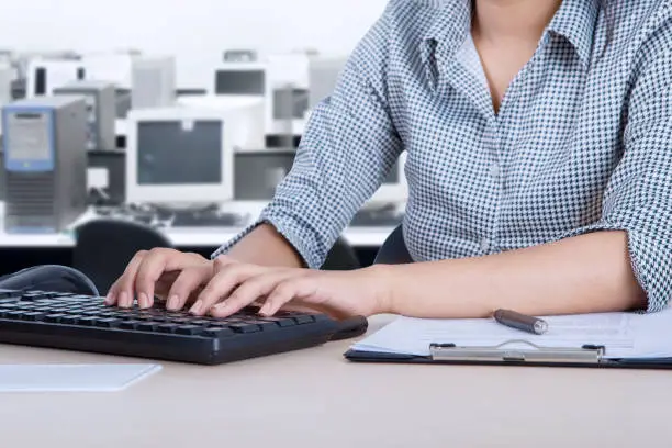 Closeup of a female employee working with a computer and clipboard on the desk while sitting in the office