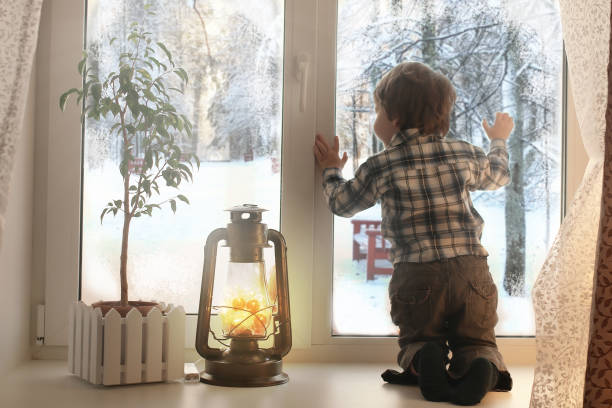 istock boy sitting on a white window sill and looks out the window 667396946