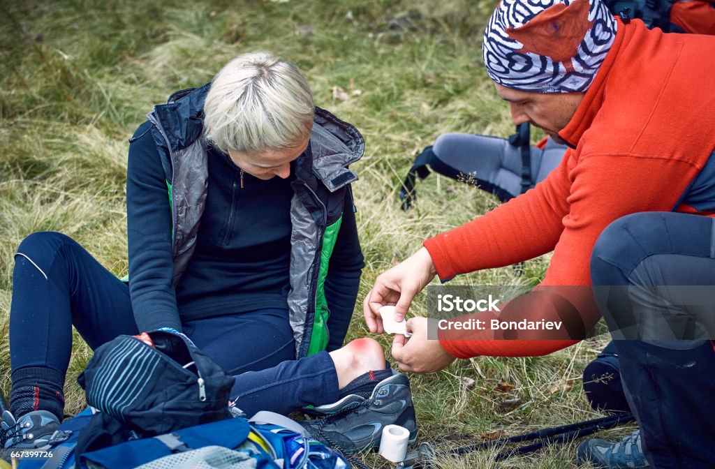 Hiking in the mountains, helping the girl on the spot. Summer trekking in the mountains, rendering assistance on the spot. First Aid Kit Stock Photo