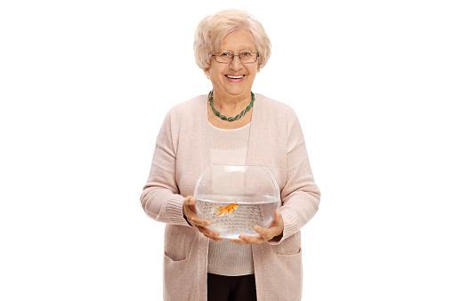 Mature woman holding a bowl with a goldfish inside and looking at the camera isolated on white background