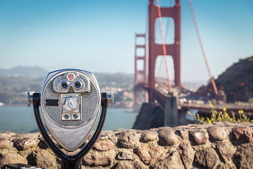 Classic view of coin operated binoculars with famous Golden Gate Bridge in the background on a beautiful sunny day with blue sky and clouds in summer, San Francisco Bay Area, California, USA