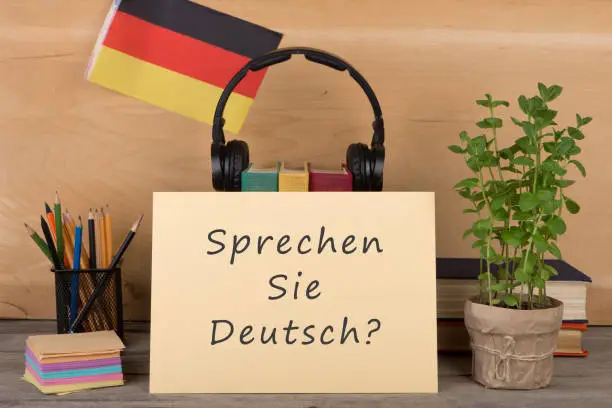 Learning languages concept - paper with text "sprechen sie deutsch?", flag of the Germany, books, headphones, pencils on wooden background