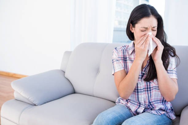 istock Pretty brunette sneezing on tissue on couch 667438900