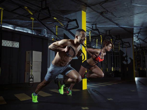 Young athletic couple doing push ups with trx straps in a modern gym. Woman is wearing unbranded clothes.
