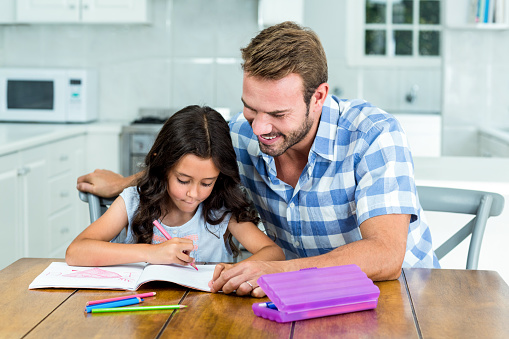Father looking at daughter while drawing in book at home