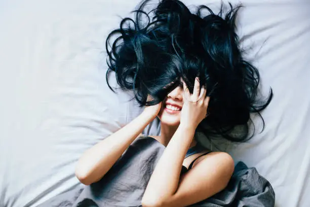 Happy young woman laughing in bed, hair covering the face.