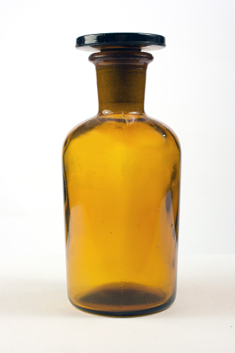 Science acid or strong chemical bottle with glass lid, light background.