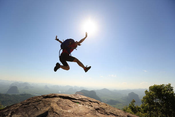 istock cheering successful young woman hiker jumping on mountain peak 667462078