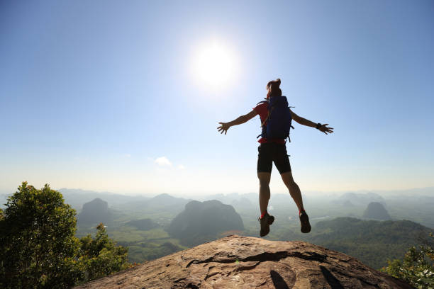 istock cheering successful young woman hiker jumping on mountain peak 667464828