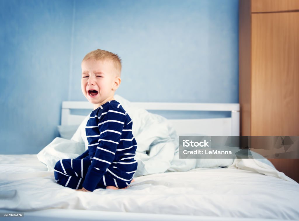 Sleepy boy sitting in bed Sleepy boy sitting in bed and crying. Tired child in bedroom Child Stock Photo