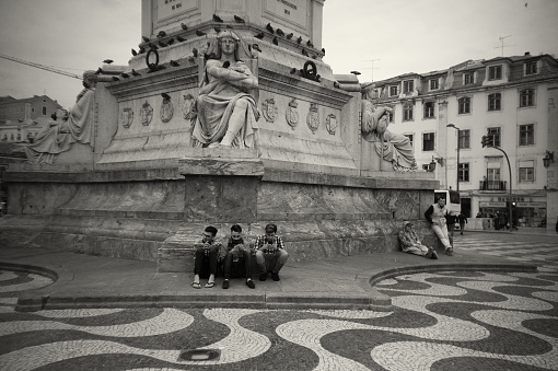 Lisbon, Portugal - Mars 14, 2017: Three young men text on their cell phones while resting in the Rossio Square in Lisbon downtown.