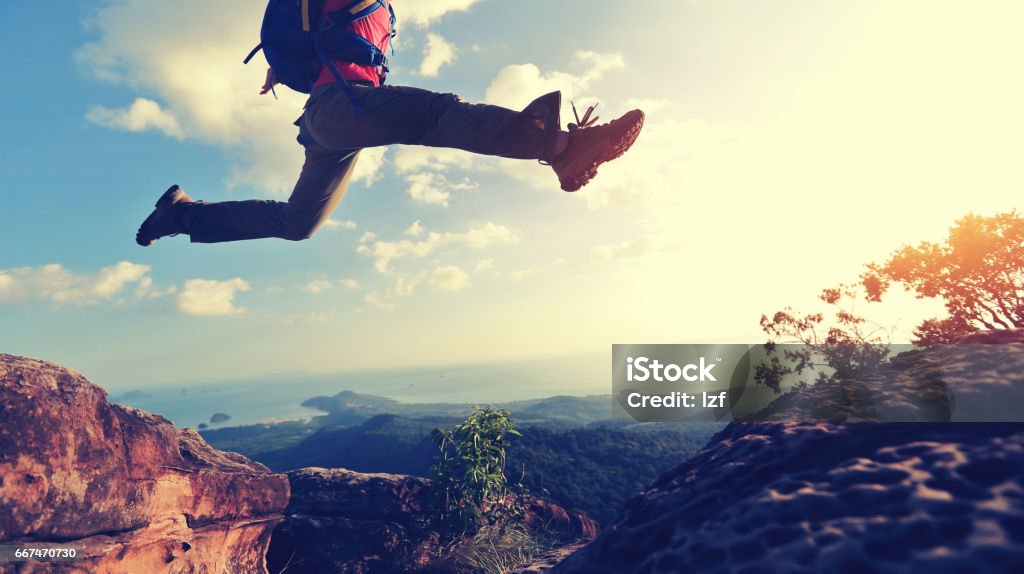 jumping over precipice between two rocky mountains at sunset jumping over precipice between two rocky mountains at sunset. freedom, risk, challenge, success concept Jumping Stock Photo