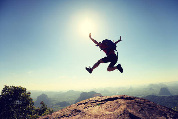 istock cheering successful young woman hiker jumping on mountain peak 667477360