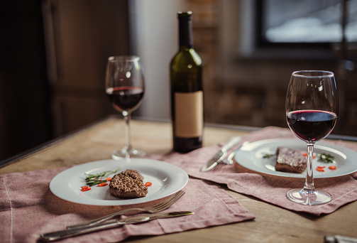 Red wine in glasses with wine bottle and delicious steaks on plates