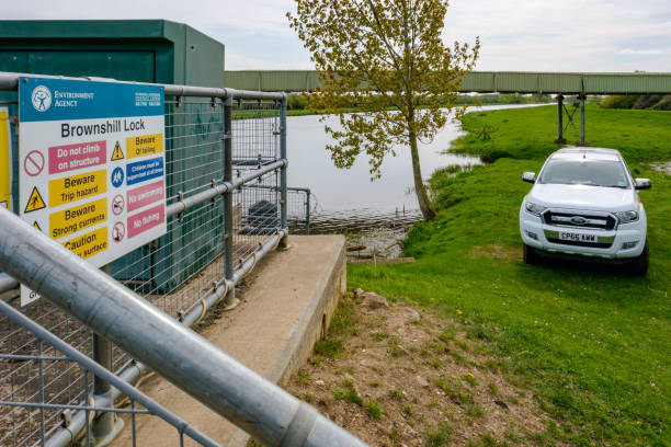 Saint Ives, Cambridgeshire, UK - April 11 2017: Detailed view of an automated locking system, together with the associated warning signs seen next to a narrow bridge crossing the lock. Detailed view of an automated locking system, together with the associated warning signs seen next to a narrow bridge crossing the lock. Also in view is a white 4x4 truck, used by an environment agency for rivers protection. ford crossing stock pictures, royalty-free photos & images
