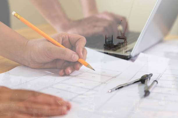 istock Architect or engineer meeting, working with blueprints and laptop in office, double exposure with crane and building under construction 667486710