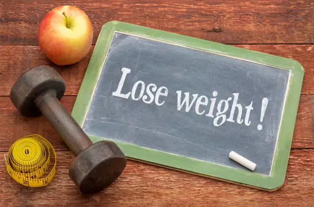 Lose weight concept -  slate blackboard sign against weathered red painted barn wood with a dumbbell, apple and tape measure