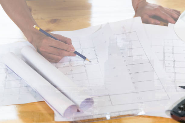 istock Architect or engineer working with blueprints in office, double exposure with crane and building under construction 667491938