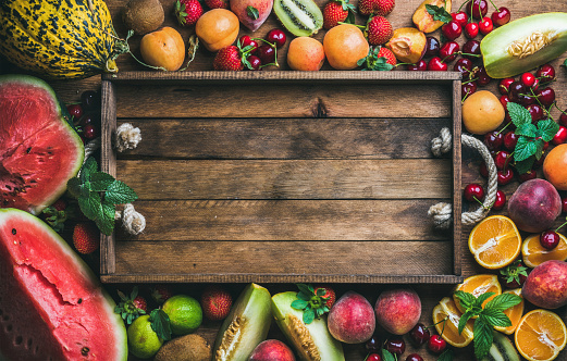 Summer fresh fruit variety with rustic wooden tray in center, top view, copy space, horizontal composition