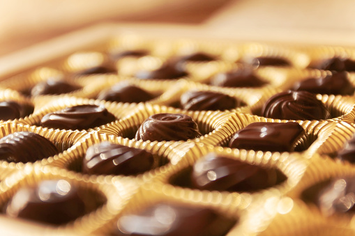 Chocolate candies of different shapes in a gold box, a perspective view and blur.