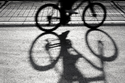 Blurry silhouette and shadow of a cyclist on a proteted bike path in sunset in black and white