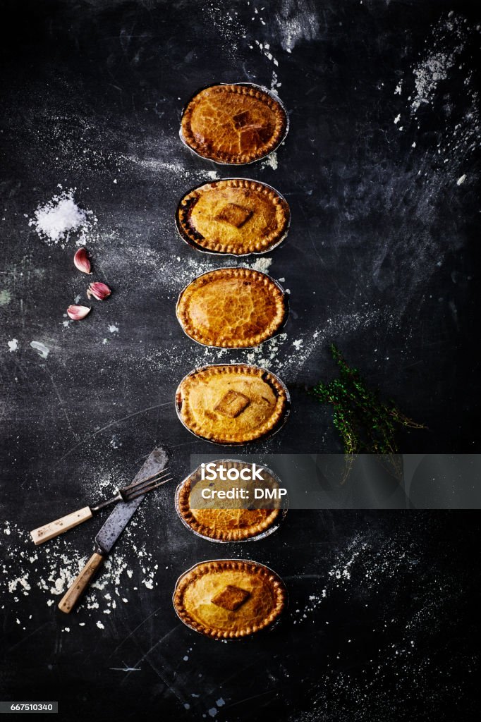 Varieties of meat and vegetarian pies on table Top view of different meat pies and vegetarian pies on black table with knife, fork and seasonings Meat Pie Stock Photo