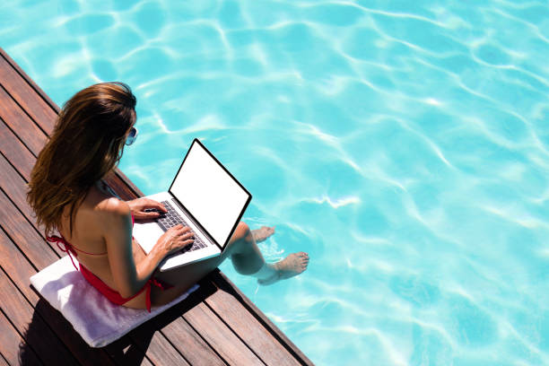 istock Woman using her laptop on the pool edge 667539654