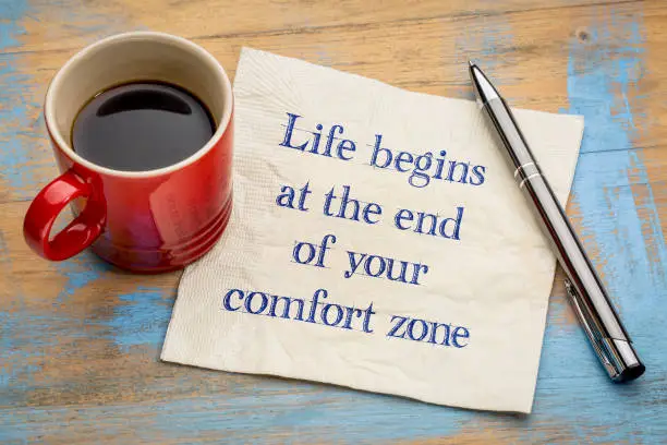 Life begins at the end of your comfort zone - inspirational handwriting on a napkin with a cup of coffee