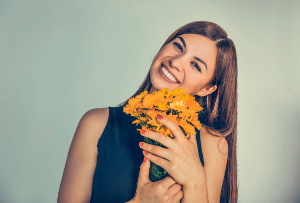 Beautiful smiling girl, woman holding bouquet of marigold, calendula. Young smiley cute female lady smelling flowers isolated on green background wall. Positive facial expression human emotion feeling Beautiful smiling girl, woman holding bouquet of marigold, calendula. Young smiley cute female lady smelling flowers isolated on green background wall. Positive facial expression human emotion feeling pot marigold stock pictures, royalty-free photos & images