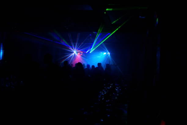 istock Deejay silhouette on a stage with big disco ball at background with the colorful rays on it 667551222