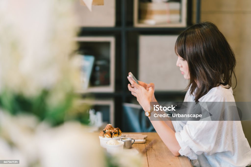 Beautiful Asian girl using smartphone at cafe with chocolate toast, ice cream, and milk syrup. Coffee shop dessert and modern casual lifestyle or mobile phone technology concept. With copy space Social Media Stock Photo