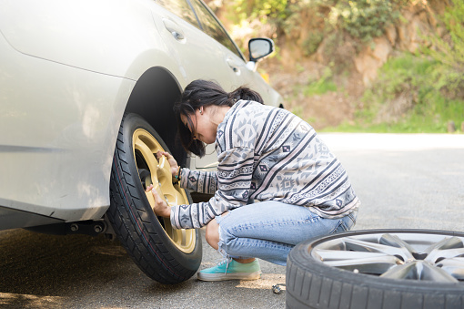 A young hispanic women stranded on the side of the road changing a flat tire.A young hispanic women stranded on the side of the road changing a flat tire.