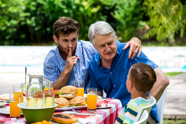 istock Man gesturing silence while son talking with grandfather at lawn 667579578