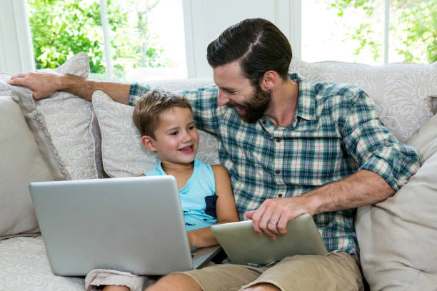 istock Happy father sitting by son with laptop on sofa 667587930