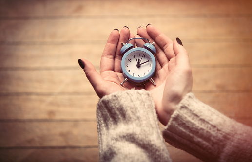 beautiful woman hands holding small blue alarm clock on the wonderful brown wooden background