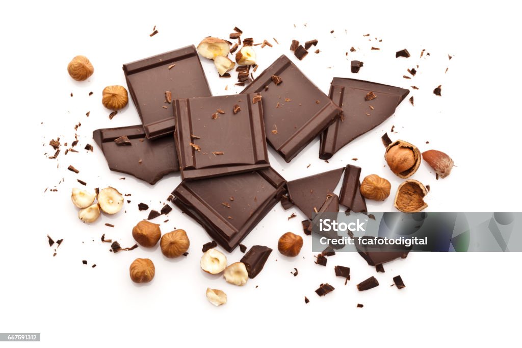 Chocolate pieces and hazelnuts isolated on white background Top view of chocolate pieces with peeled hazelnuts isolated on white background. Some chocolate shavings are sparse in the composition. Predominant colors are brown and white. DSRL high key studio photo taken with Canon EOS 5D Mk II and Canon EF 100mm f/2.8L Macro IS USM Hazelnut Stock Photo