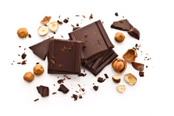 Top view of chocolate pieces with peeled hazelnuts isolated on white background. Some chocolate shavings are sparse in the composition. Predominant colors are brown and white. DSRL high key studio photo taken with Canon EOS 5D Mk II and Canon EF 100mm f/2.8L Macro IS USM