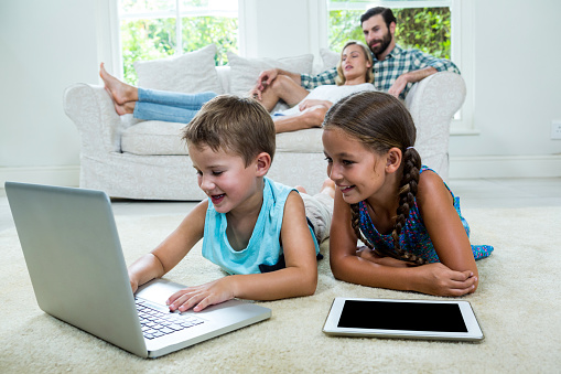 Children using laptop in front of parents on sofa at home