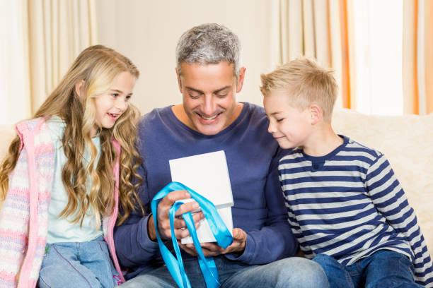 istock Father opening gift given by children on sofa 667595402