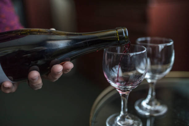 istock Unrecognizable woman pouring red wine, from a bottle, into two glasses. 667598936