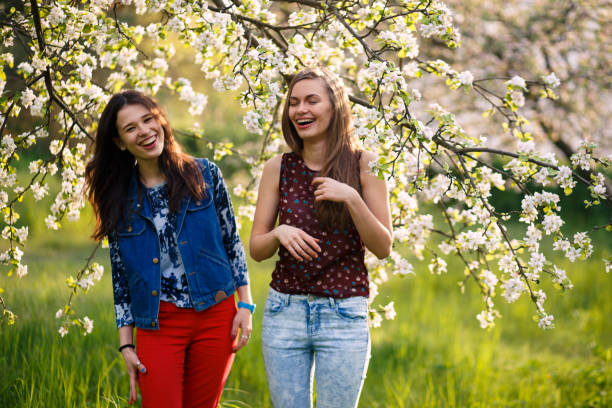 Two Young Women Enjoying The Scent Of Blossoming Tree – Free Stock Photo