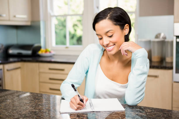 Smiling brunette writing on note pad Smiling brunette writing on note pad in the kitchen shopping list stock pictures, royalty-free photos & images