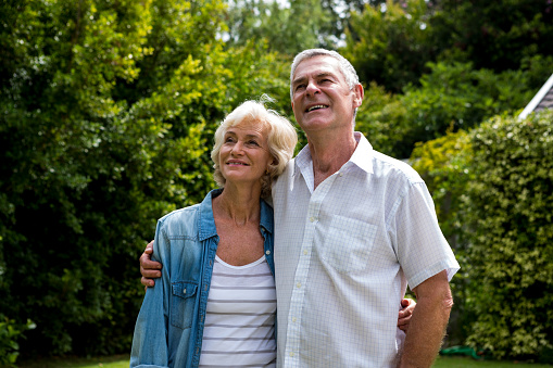 Thoughtful senior couple looking up against plants in back yard