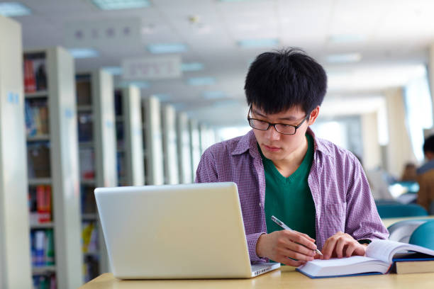 istock One male asian college student study in the library with laptop on table 667632862